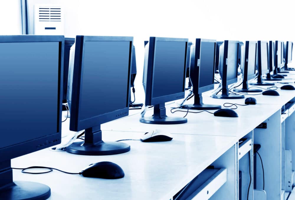 A row of idle high-performance workstations with monitors, keyboards, and mice in a bright, empty office or computer lab environment.