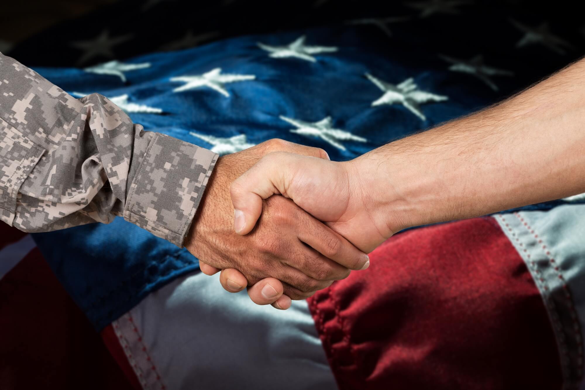 A person in military uniform shakes hands with a civilian, with a United States flag in the background, commemorating the signing of the $5 billion ADMC-3 Army contract.