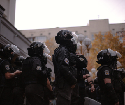 Group of law enforcement officers in helmets and protective gear assembled outside a building, facing various directions.
