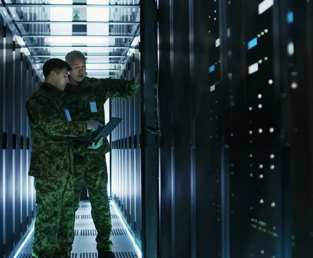 Two military men in camouflage standing in a secured server room.