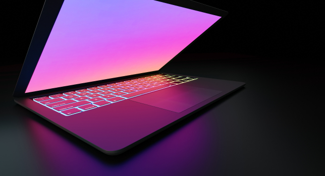 An open laptop with a glowing keyboard displaying pink and purple lights on a dark, federal background.